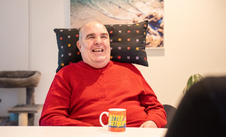 Disabled man laughing and chatting whilst drinking a tea