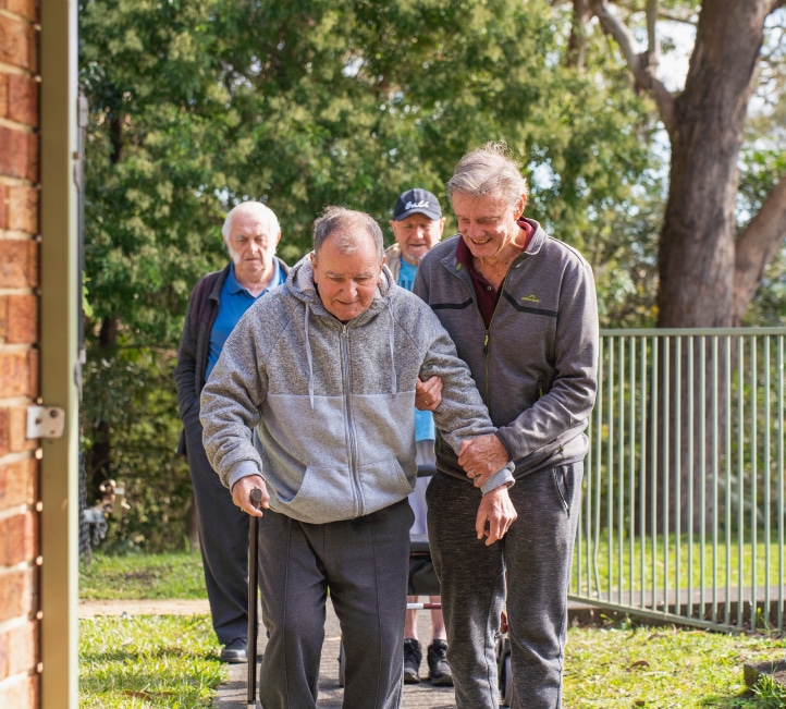 Elderly man with a walking stick being assisted by friends