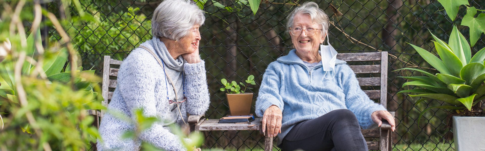 Two elderly female friends sitting chatting in a garden